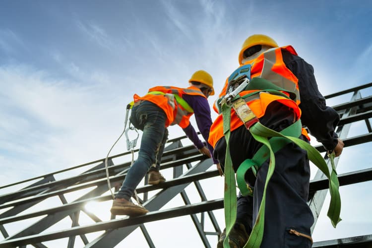 Two workers in hi-vis and hard hats climbing a steel scaffold in fall-arrest harnesses