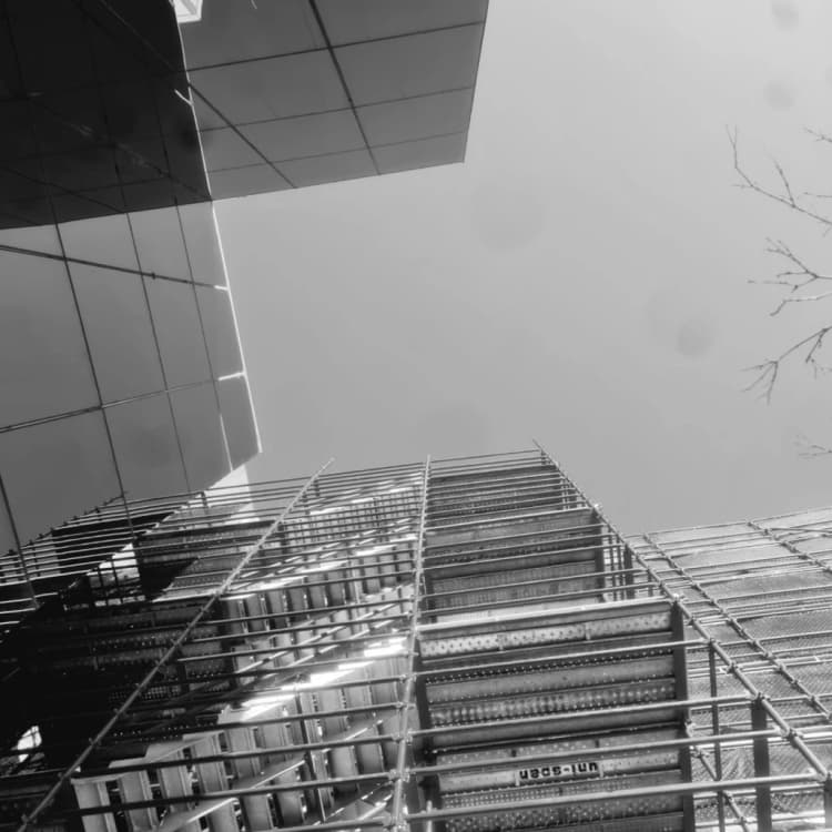 A low-angle black-and-white view up a scaffold against a glass building facade