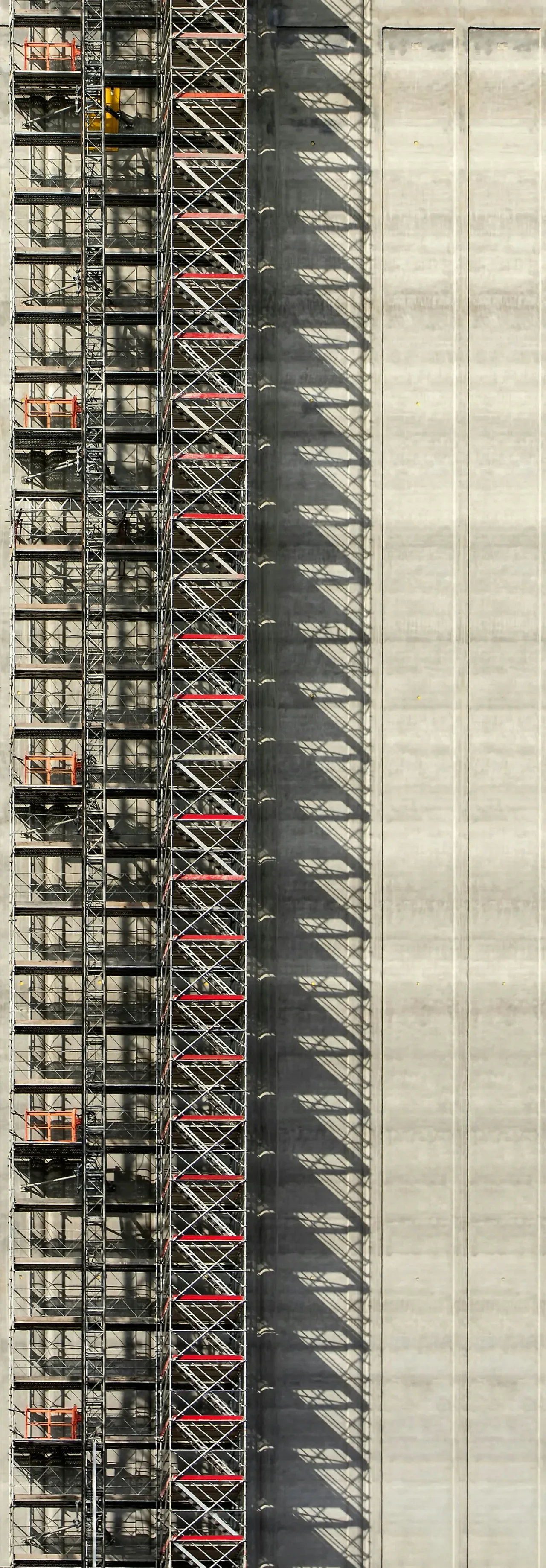 A tall multi-storey stair-tower scaffold rising up a concrete building facade
